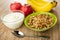 Apples, bananas, bowl with yogurt, bowl with granola, spoon on wooden table