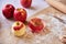 Apples, rolling pin, flour, parchment paper on the table. Woman`s hands peeling an apple. Preparation for cooking pastry