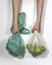 Apples in a string bag and a green plastic bag in female hands on a white background