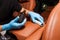 Applying a nano-ceramic coating for interior leather on the car`s seat brown upholstery by a worker in blue gloves with a sponge