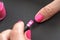 Applying pink nail polish - closeup photo of woman fingernail and little brush with paint on gray black background