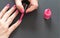 Applying pink nail polish - closeup photo of woman hands, little brush, small bottle and fingernails on gray / black background