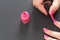 Applying pink nail polish - closeup photo of woman hands, little brush, varnish bottle and fingernails on gray black