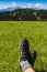 Approach shoes on the feet of a tourist resting during a trip on green grass in a clearing with a view of the mountain ridge