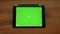 Approaching close-up horizontal view of tablet with green screen on wooden desk background.