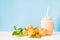 Apricot milkshake decorated with fresh apricots and green leaves on white and blue background