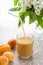 Apricots and fruit smoothie in glass on patterned linen tablecloth and white lilac.