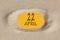 April 22. 22th day of the month, calendar date. Hole in sand. Yellow background is visible through hole