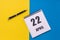 April 22th. Day of 22 month, calendar date. A notebook with a spiral and a pen lies on a yellow-blue background, flat lay, copy