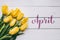 April hand lettering calligraphy. Yellow tulips bunch on white wooden planks rustic barn rural table background. Letters,