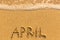 April - written by hand on a golden beach sand. Calendar.