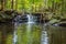 Apshawa Falls in a suburban nature preserve in NJ is surrounded by lush green forest on a summer afternoon