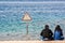 Aqaba, Jordan - January 24, 2016. Couple sitting on the shore of Red Sea with caution signboard