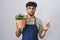 Arab man with beard holding green plant pot pointing with hand finger to the side showing advertisement, serious and calm face