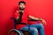 Arab man with beard sitting on wheelchair looking at the camera blowing a kiss with hand on air being lovely and sexy