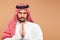 An Arab man in national dress is praying on a beige background. Dishdasha, kandora, thobe ,, traditional men`s clothing of the