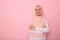 Arab Muslim woman wearing a hijab crossing arms, smiling with beautiful toothy smile, poses on pink background with copy space