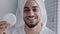 Arabian hispanic indian man with towel on head holding jar of cream for face laugh looking at camera recommend natural