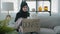 Arabian Islamic Muslim female in black hijab kind woman volunteer at home sitting on couch packing donations box with