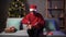Arabic man in Christmas Santa hat packages delivery box with gift, packing parcel package on couch at home Xmas tree