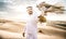 Arabic man with traditional emirates clothes walking in the desert with his falcon bird