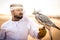 Arabic man with traditional emirates clothes walking in the desert with his falcon bird