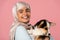 Arabic young woman in hijab holding cute corgi puppy, isolated on pink