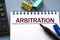 ARBITRATION word is written in a notebook with a marker, calculator, clamps and cactus