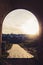 Arch facing the brick pavement leading to a village during sunset