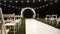 Arch for a wedding ceremony with white chairs and a white wooden walkway.