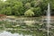 An arched bridge over a lake leading to walking trails though a forest and around the lake with a fountain in Wisconsin