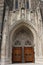 The arched entryway of the Duke University Chapel, carved from stone with statues and intricate details and two wood doors