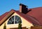 Arched window and brick chimney on the red metal tile roof under blue sky, house exterior