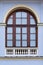 Arched window with wooden frame and decorative white fence on bottom on a facade of blue ancient building