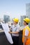 Architect And Construction Worker Talking and Looking at Blueprint On Rooftop, City in the background