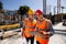 Architect and structural engineer dressed in orange work vests and helmets discuss a building project on the tablet on