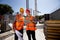 Architect and structural engineer dressed in orange work vests and helmets discuss a building project on the tablet on