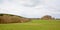 Ardennes landscape with green maedows and layers of bare deciduous and pine trees under a cloudy sky