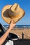 Arm in car holding straw hat at coast
