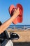 Arm in car showing bath slippers at sea