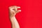 Arm of caucasian white young man over red isolated background picking and taking invisible thing, holding object with fingers