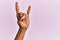 Arm and hand of black middle age woman over pink isolated background gesturing rock and roll symbol, showing obscene horns gesture