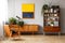 Armchair next to wooden cupboard with plants in retro flat interior with painting. Real photo