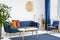 Armchair and sofa in blue and orange living room interior with lamp above wooden table. Real photo