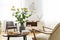 Armchair at table with flowers, books and food in bright apartment interior with windows. Real photo