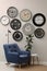 Armchair, table and many different clocks hanging on white wall in room