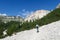 Armentarola - A woman with a hiking backpack hiking on a gravelled road in high Italian Dolomites. There is a dence forest