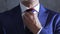 Arms of person in blue suit straightens necktie on neck on background of gray concrete wall