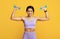 Arms workout. Portrait of fit black sportswoman doing biceps exercises with two dumbbells over yellow background