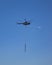 Army Soldiers Hanging From Helicopter against clear sky.